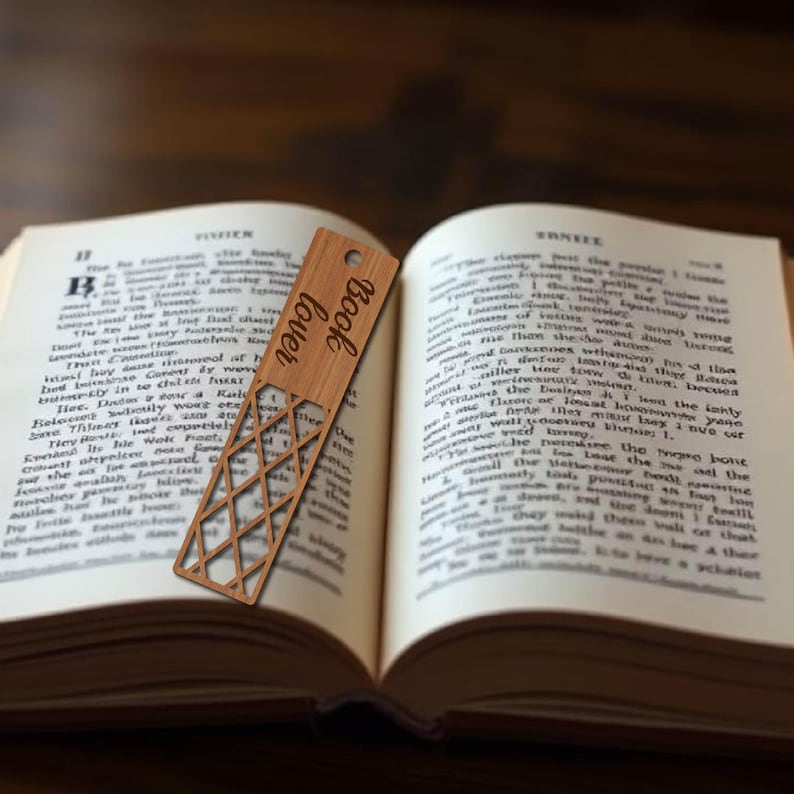 K&ouml;nnte beinhalten: Ein Holz-Lesezeichen mit geometrischem Design und den eingravierten Worten "Book Lover". Das Lesezeichen befindet sich in einem ge&ouml;ffneten Buch.