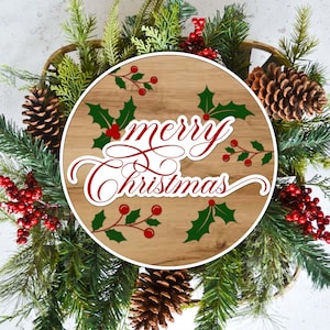 May include: A Christmas wreath with a wooden center displaying the words "Merry Christmas" in red script. The wreath is decorated with green pine needles, red berries, holly leaves, and pine cones.