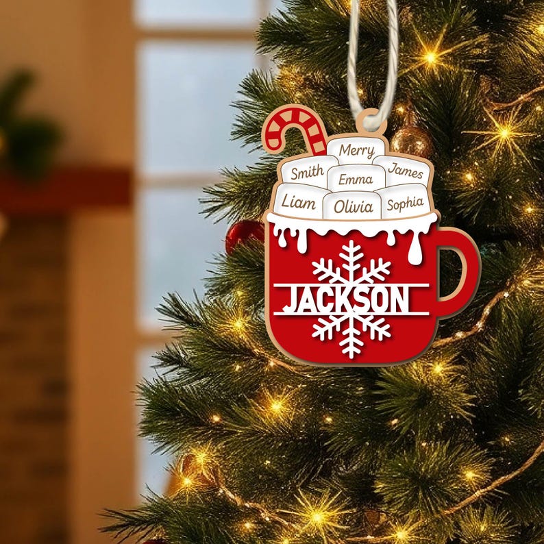 May include: A red and white Christmas ornament shaped like a mug, with the name "Jackson" and a snowflake design. The ornament includes names like Smith, Emma, and Liam. A candy cane and the word "Merry" are also visible.