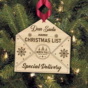 K&ouml;nnte beinhalten: Weihnachtsbaumschmuck aus Holz in Form eines Umschlags mit dem Text "Lieber Weihnachtsmann Name WEIHNACHTSLISTE Sonderzustellung" und einem kleinen Stempel mit der Aufschrift "Nordpol Postdienst".
