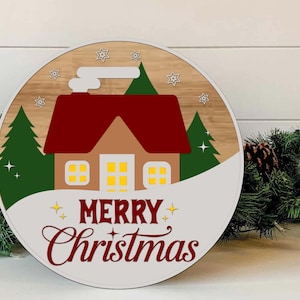 May include: A round Christmas decoration featuring a house with a red roof, green trees, and the words "MERRY Christmas" in a festive font. The design is set against a wood-grain background with a white border and star accents.