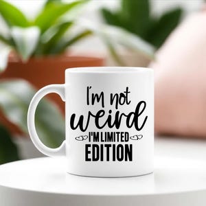 May include: White ceramic coffee mug with a black design that reads "I'm not weird I'm limited edition" with two small hearts on either side of the text.
