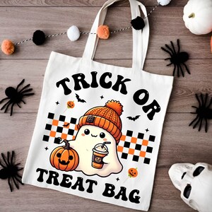 May include: White canvas tote bag with black text that reads "Trick or Treat Bag". A cartoon ghost wearing a beanie hat and holding a pumpkin spice latte is in the center of the bag.
