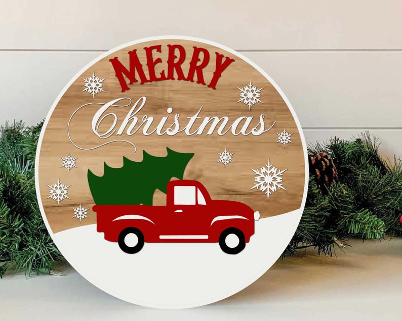 May include: Round wooden Christmas sign with a red truck carrying a green Christmas tree. The sign has the words "MERRY Christmas" in red and white, with white snowflakes. The background is a wood grain pattern.