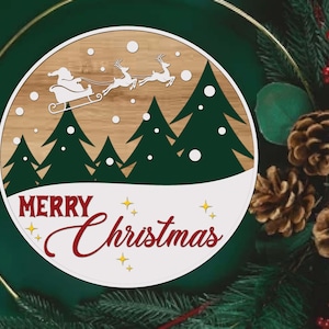 May include: A round wooden Christmas decoration featuring a laser-cut design of Santa Claus in a sleigh pulled by reindeer above green trees. The words "Merry Christmas" are written in red script with yellow star accents.