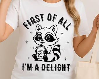 May include: White t-shirt featuring a cartoon raccoon drinking from a cup with a skull and crossbones. The text "FIRST OF ALL I'M A DELIGHT" is printed above and below the raccoon illustration. Four small star shapes are on the shirt.