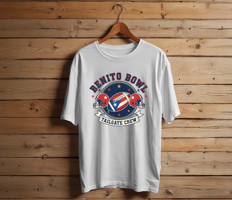 May include: White t-shirt with a graphic featuring a football, two helmets, and the text "Benito Bowl Tailgate Crew." The design incorporates red, white, and blue colors, with stars and a banner.