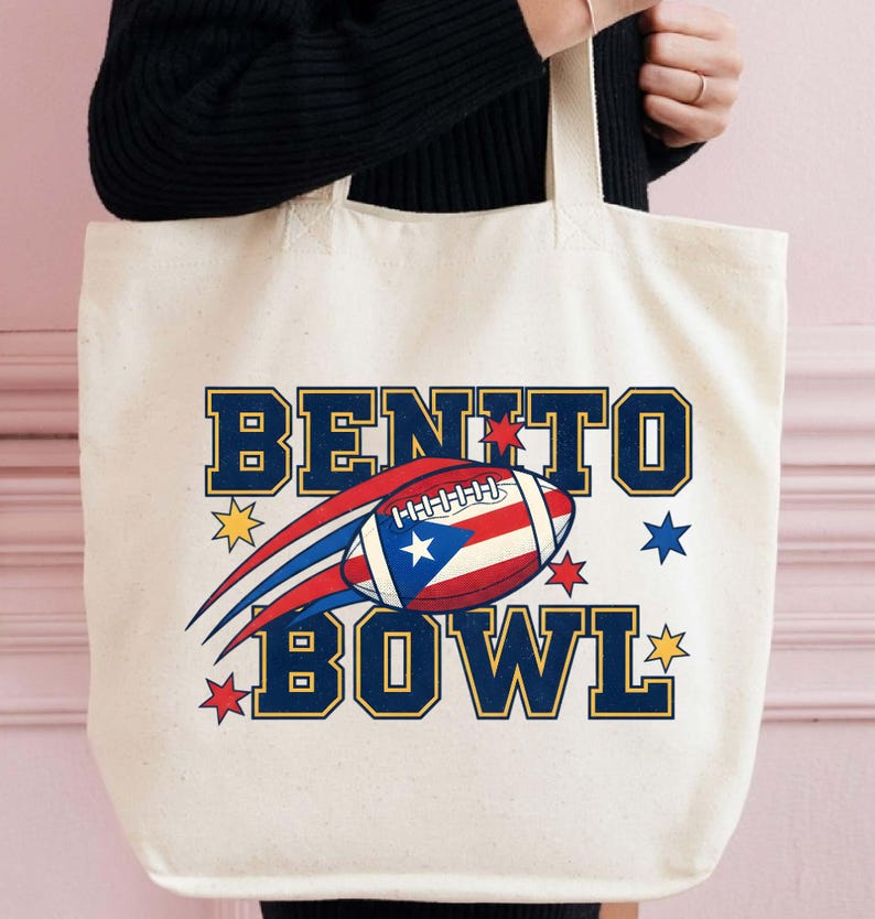 May include: Cream-colored tote bag with the words "BENITO BOWL" in navy blue block letters with gold trim. A football with the Puerto Rican flag design is in the center. Red, blue, and gold star graphics surround the text and football.
