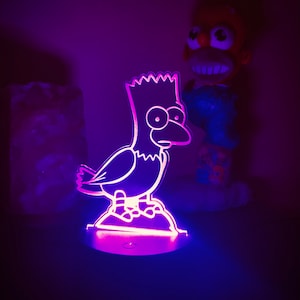 May include: A purple and blue light-up nightlight shaped like a cartoon bird with a yellow head and a black outline. The bird is standing on a white base.