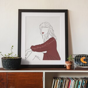 May include: Framed art print featuring a line drawing of a person in a maroon dress, with the text "long story short I survived" in cursive. The artwork is in a black frame and displayed on a wooden shelf.