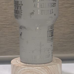 Może przedstawiać: Mrożony kubek z wytrawionymi wzorami i tekstem, w tym "We're Having An All Night Revival" i "Small Town Smoke Show". Kubek stoi na jasnej drewnianej podstawce. Projekt zawiera gwiazdy, kapelusz kowbojski i konia.