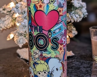 May include: A stainless steel tumbler with a colorful design featuring 80s pop culture icons like My Little Pony, Care Bears, and the Teenage Mutant Ninja Turtles. The tumbler has a heart with the text "I Love the 80s" and a rainbow.