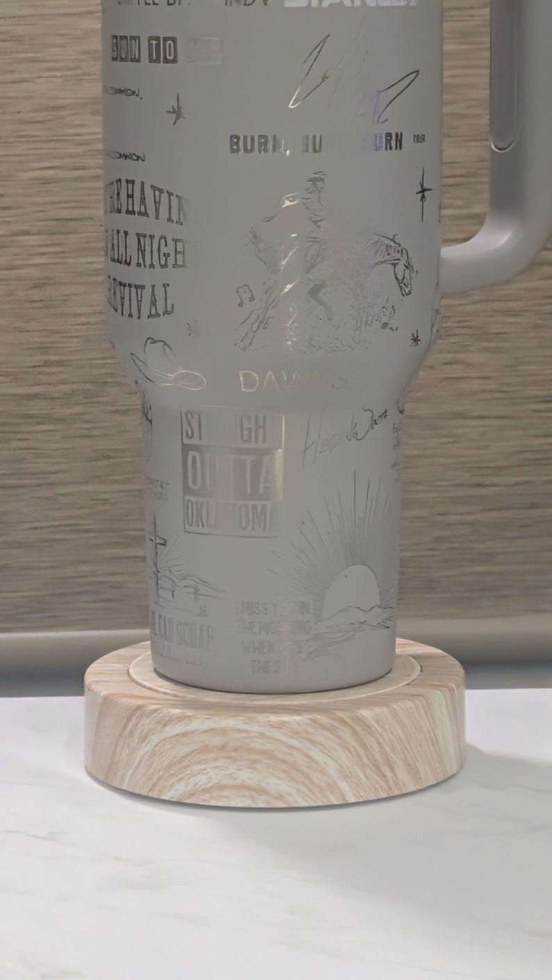 Może przedstawiać: Jasnoszary kubek z wytrawionymi wzorami i tekstem, w tym "Burn, Burn, Burn" i "Straight Outta Oklahoma". Kubek stoi na jasnej drewnianej podstawce. Uchwyt jest jasnoszary.