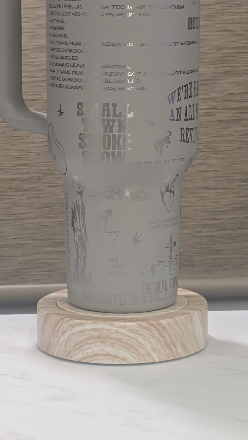 Może przedstawiać: Biały kubek z wytrawionymi ilustracjami i tekstem, w tym słowami "Small Town Smoke" i "We're an Alley Review". Kubek stoi na jasnej drewnianej podstawce.