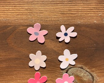 May include: Six flower stickers on a wooden surface. The stickers are in pink, white, and light blue with different coloured centres.