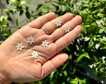 May include: Six small white paper daisies with yellow centres are displayed on a person's hand. The daisies are arranged in a semi-circle.