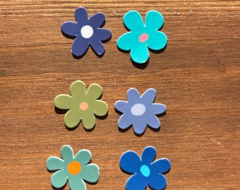 May include: Six colourful flower stickers with different coloured centres and outlines. The stickers are on a wood background.
