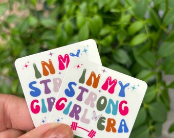 May include: Two white square stickers with the text "In My Strong Girl Era" in colourful, bubbly letters. The stickers feature a butterfly and a barbell.
