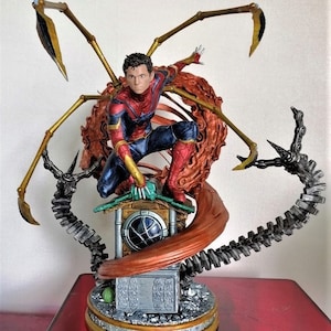 May include: A red and blue Spider-Man action figure with gold web shooters, standing on a rooftop with a red and brown web. The figure is part of a larger diorama with a metallic gray and black base.