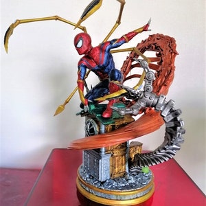 May include: A red and blue Spider-Man action figure with gold web shooters, standing on a detailed base with a metallic red and gray mechanical arm. The figure is posed in a dynamic action pose.
