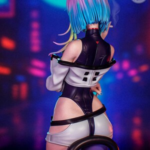 May include: A detailed figure of a woman with vibrant blue, pink, and yellow hair, wearing a futuristic black and white outfit. The figure is holding a cigarette, with smoke rising. The background is a blurred neon cityscape.