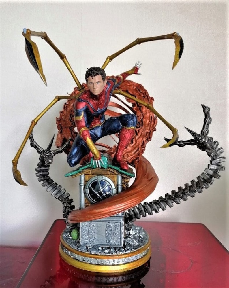 May include: A red and blue Spider-Man action figure with gold web shooters, standing on a rooftop with a red and brown web. The figure is part of a larger diorama with a metallic gray and black base.
