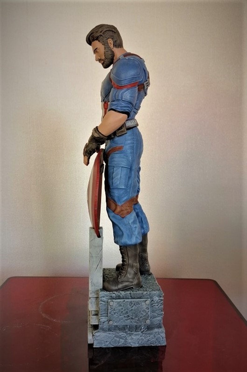 May include: A detailed figurine of Captain America in his blue and red costume, holding his shield. The figurine is standing on a stone base.