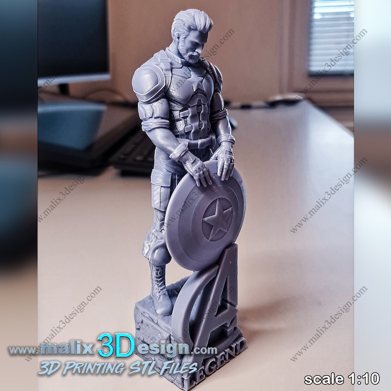 May include: A gray 3D printed figurine of Captain America standing with his shield in his left hand. The base of the figurine is a gray 3D printed base with the Avengers logo and the word "LEGEND" printed on it.