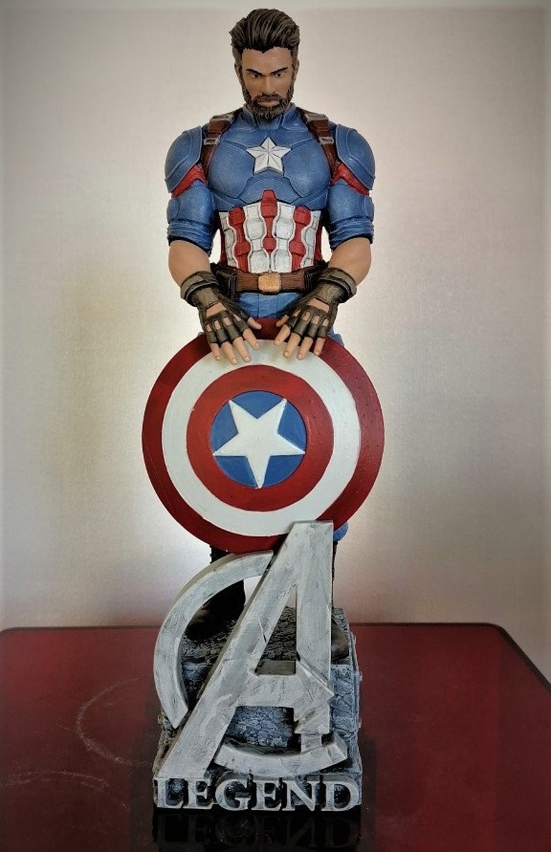 May include: A Captain America action figure with a red, white, and blue costume, holding his shield. The figure is standing on a base with the Avengers logo and the word "LEGEND" printed on it.