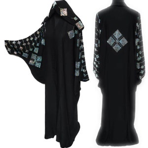 May include: A black abaya with a hood and long sleeves. The abaya is decorated with silver and iridescent rhinestones in a geometric pattern.