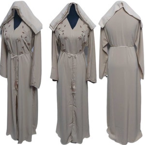 May include: A beige abaya with a hood and long sleeves. The abaya has a decorative belt and embroidery on the front.