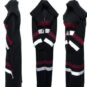 May include: Black abaya with a burgundy and white striped pattern. The abaya has a zipper down the front and a hood. The sleeves are long and have a striped pattern.