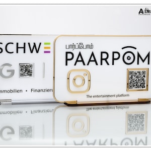 May include: Two white acrylic signs with gold trim. The left sign has the text "SCHWE" and a QR code. The right sign has the text "PAARPOM" in black and a QR code. The text "The entertainment platform" is below the QR code.