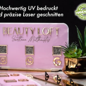 Könnte beinhalten: Ein pinkfarbenes Acrylschild mit goldenen Buchstaben, auf dem "BEAUTY LOFT" und "Swetlana Matthaupt" mit einem Herzsymbol steht. Das Schild hat drei goldene QR-Codes und Social-Media-Icons für Instagram, WhatsApp und Google.
