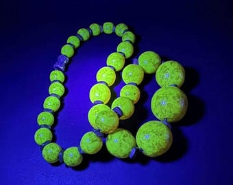 Pode incluir: Um colar com grandes contas redondas amarelas brilhantes, enfiadas em um fio preto. As contas têm uma superfície texturizada e são iluminadas contra um fundo azul escuro. Uma peça de joalheria única.