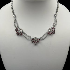 May include: A silver necklace with a double row of clear rhinestones and three red rhinestone flower accents.