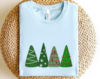 May include: A light blue t-shirt with a design of four decorated Christmas trees. The trees are green with white, red, and gold ornaments.