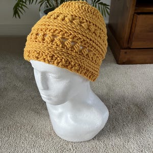 May include: A mustard yellow crocheted beanie with a stitch pattern featuring small holes throughout.