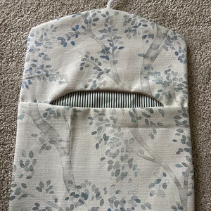 May include: A white fabric hanging organiser with a blue and grey floral pattern. The organiser has a hanger at the top and a pocket on the front.