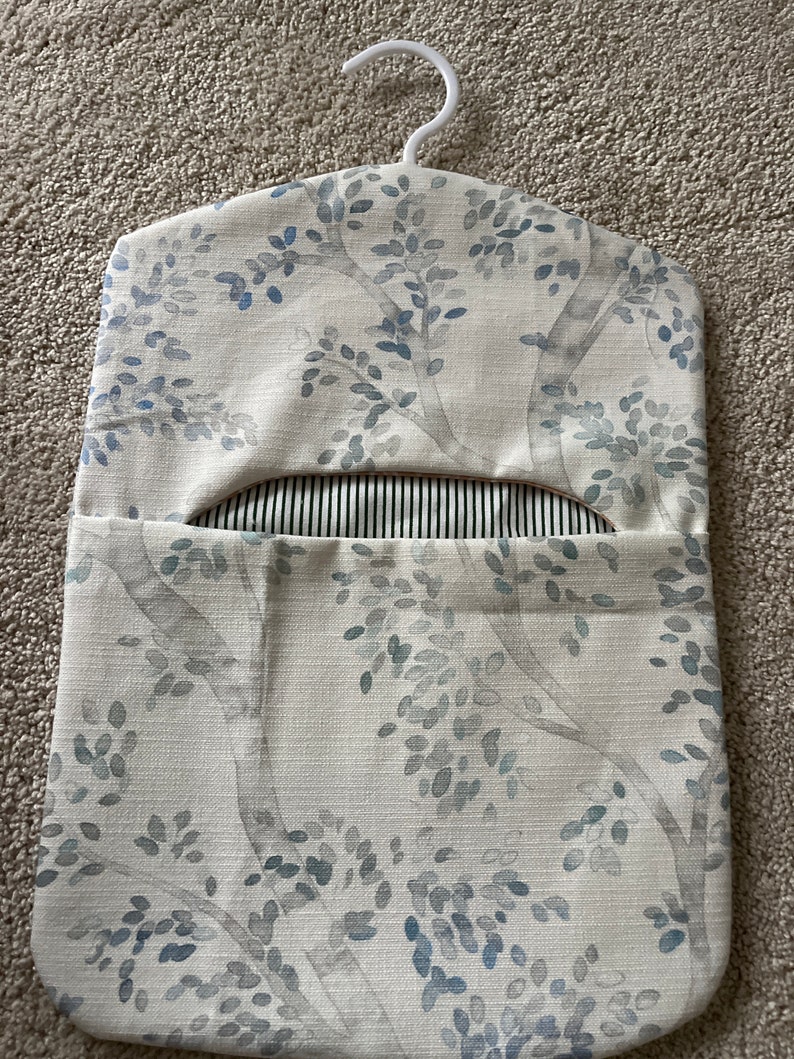 May include: A white fabric hanging organiser with a blue and grey floral pattern. The organiser has a hanger at the top and a pocket on the front.