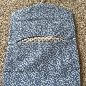 May include: A blue and white floral patterned laundry bag with a white plastic hanger. The bag has a small opening at the top for hanging clothes.