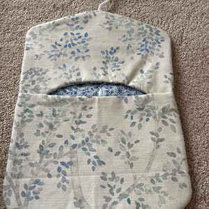 May include: A white fabric hanging organiser with a blue floral pattern. The organiser has a hanger at the top and a pocket in the front.