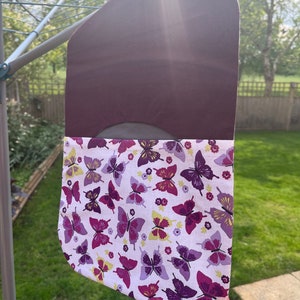 Pode incluir: Uma bolsa de tecido roxo com um forro de tecido branco com estampa de borboleta. A bolsa est&aacute; pendurada em um varal.