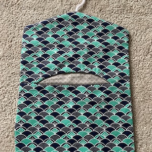 May include: A blue and green fabric garment bag with a white hanger. The bag has a repeating pattern of green and white stylised flowers on a dark blue background.