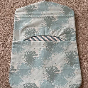 May include: A light blue hanging laundry bag with a white hanger and a white and blue striped fabric lining. The bag has a splatter paint design.