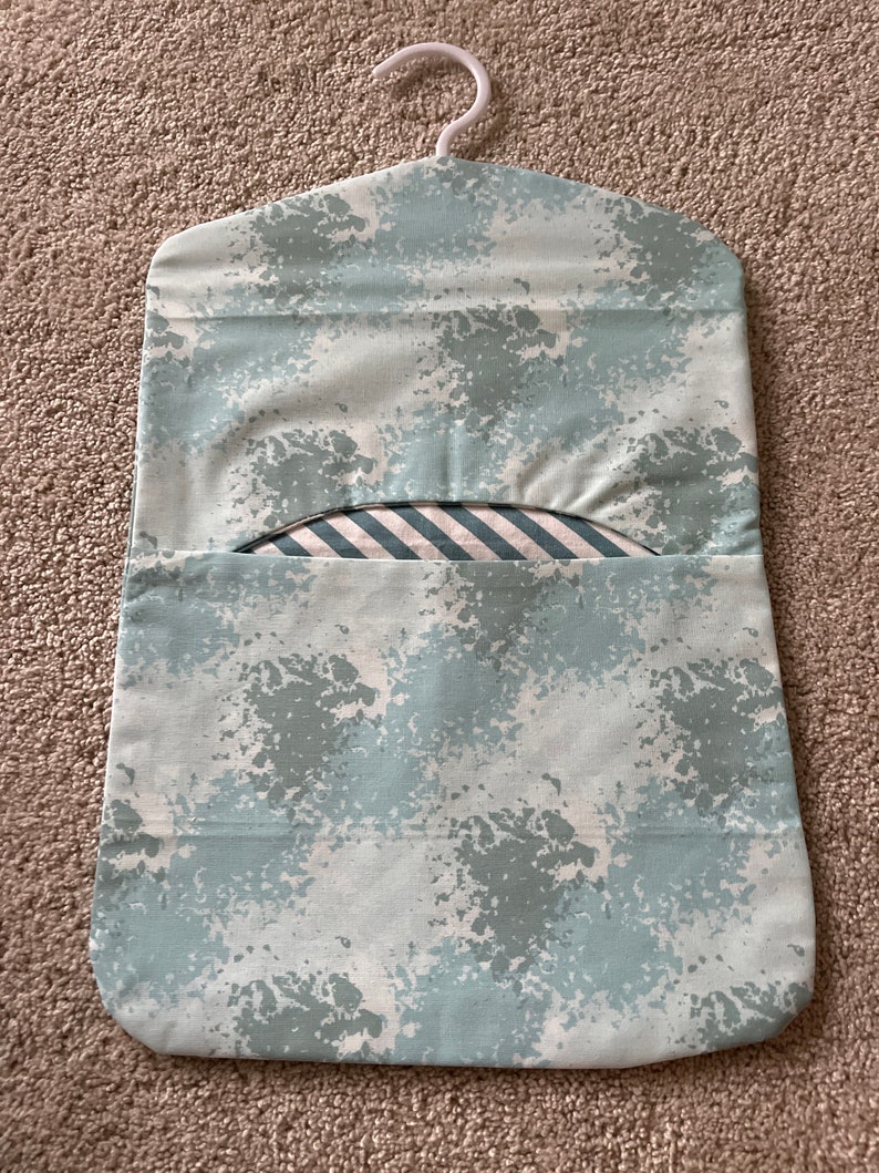 May include: A light blue hanging laundry bag with a white hanger and a white and blue striped fabric lining. The bag has a splatter paint design.