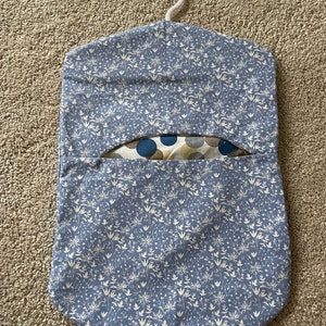 May include: A blue fabric hanging organiser with a white floral pattern. The organiser has a hanger at the top and a pocket on the front.