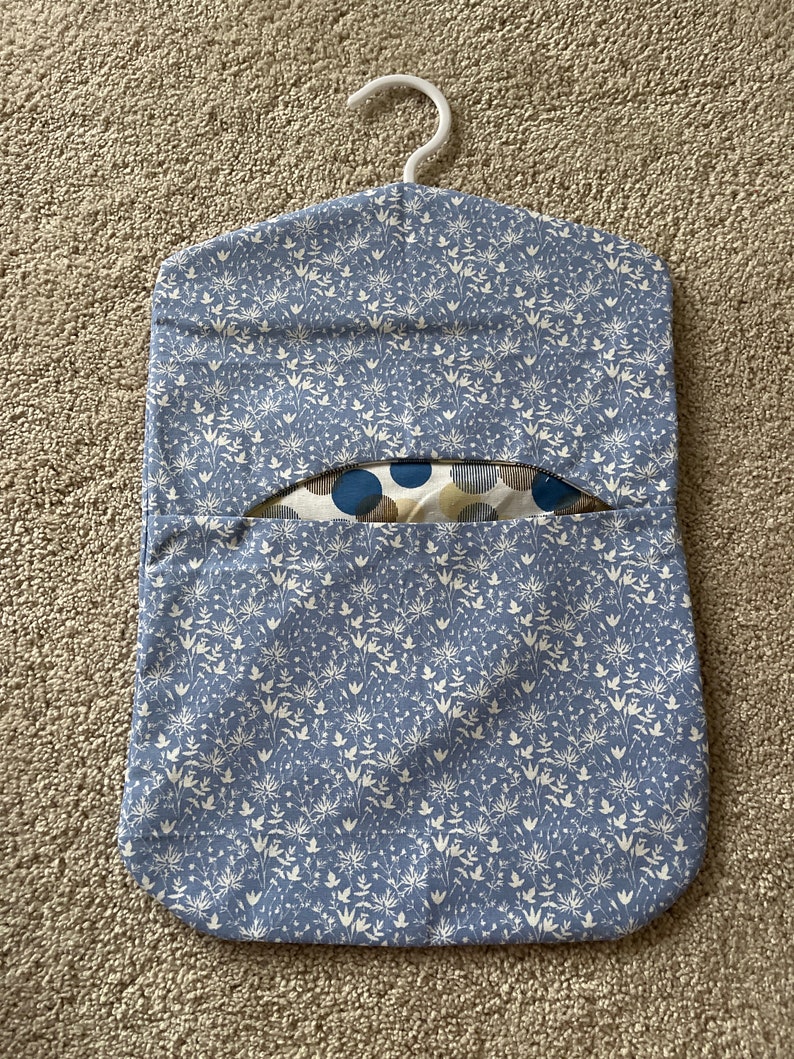 May include: A blue fabric hanging organiser with a white floral pattern. The organiser has a hanger at the top and a pocket on the front.