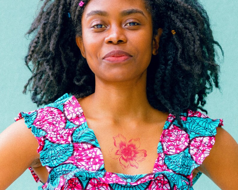 Puede incluir: Una mujer con el pelo largo y rizado oscuro que lleva un vestido estampado en rosa y azul con un tatuaje de flor roja en el pecho.