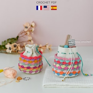 Könnte beinhalten: Zwei handgefertigte Kordelzugbeutel aus Häkelarbeit mit farbenfrohen Muschelmuster. Die Beutel sind weiß mit einem Regenbogen aus Farben und einem türkisfarbenen Kordelzug. Das Bild enthält auch den Text "zess crochet" und "CROCHET PDF".